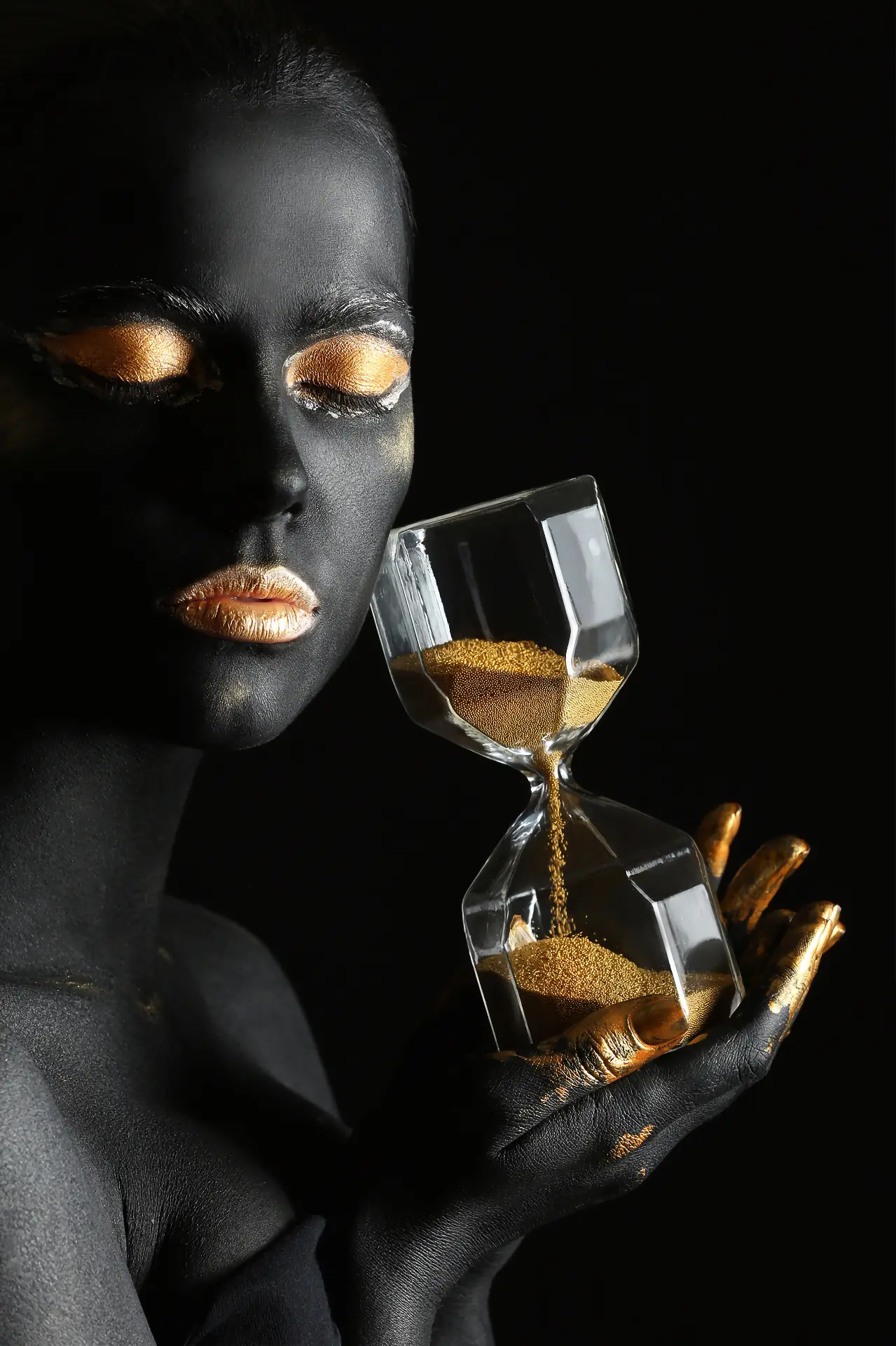 Arte preto e dourado: retrato em fundo preto com maquiagem dourada segurando uma ampulheta de vidro com areia dourada
